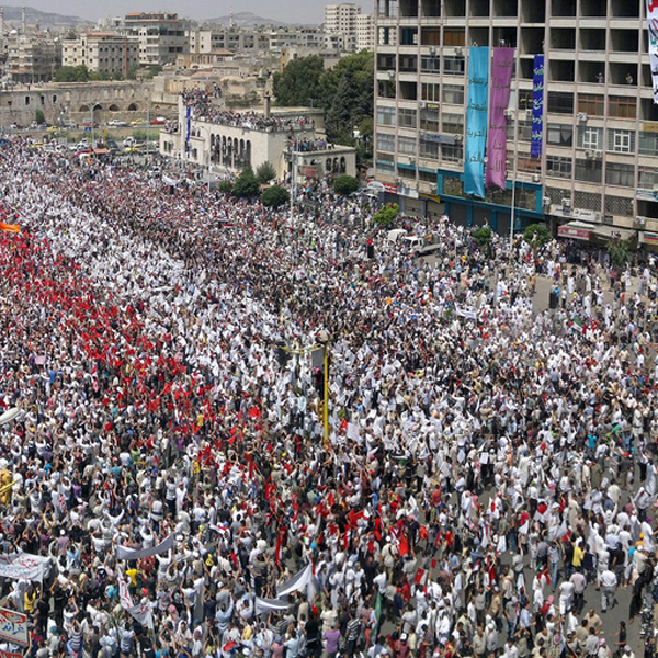 Huge protest in the street. Protestors carrying red, white, and flags to form Syrian flag