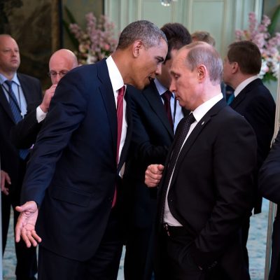 President Obama leans in close to speak something in Vladimir Putin's ear with other officials in the background.