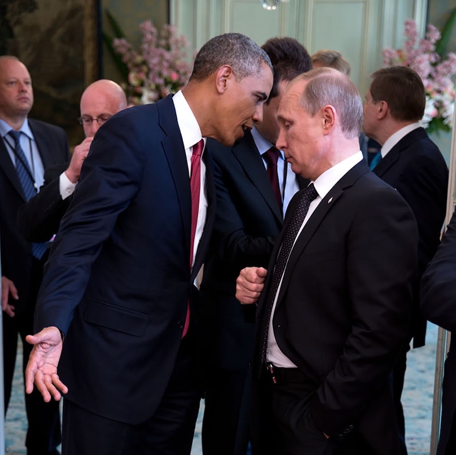 President Obama leans in close to speak something in Vladimir Putin's ear with other officials in the background.