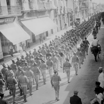 Black and white photo of lines of US troops marching down a city street