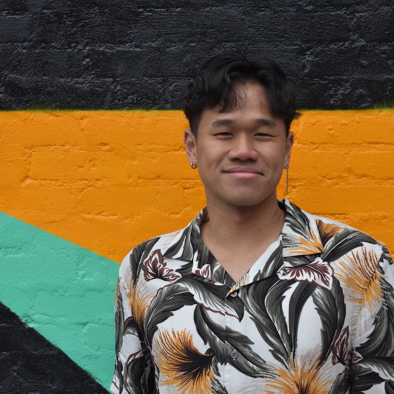 Matt Lim in front of a black, orange, and green painted brick wall.